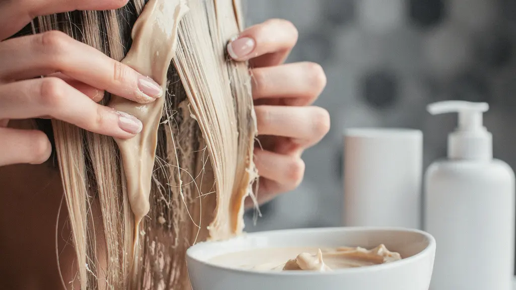 Application d'un masque capillaire sur cheveux décolorés avec texture crémeuse et mains expertes