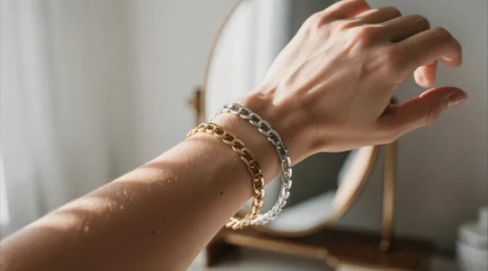 Main féminine comparant deux bracelets, un doré et un argenté, devant un miroir dans une lumière naturelle
