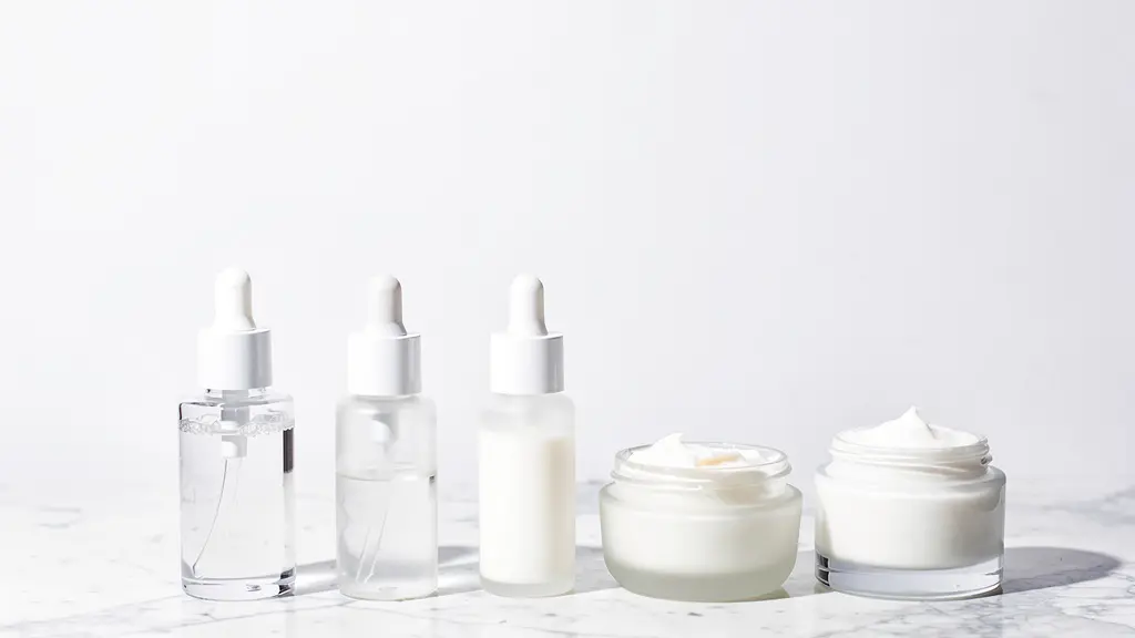 Flacons de soins cosmétiques disposés en ordre croissant de texture sur une surface de marbre blanc